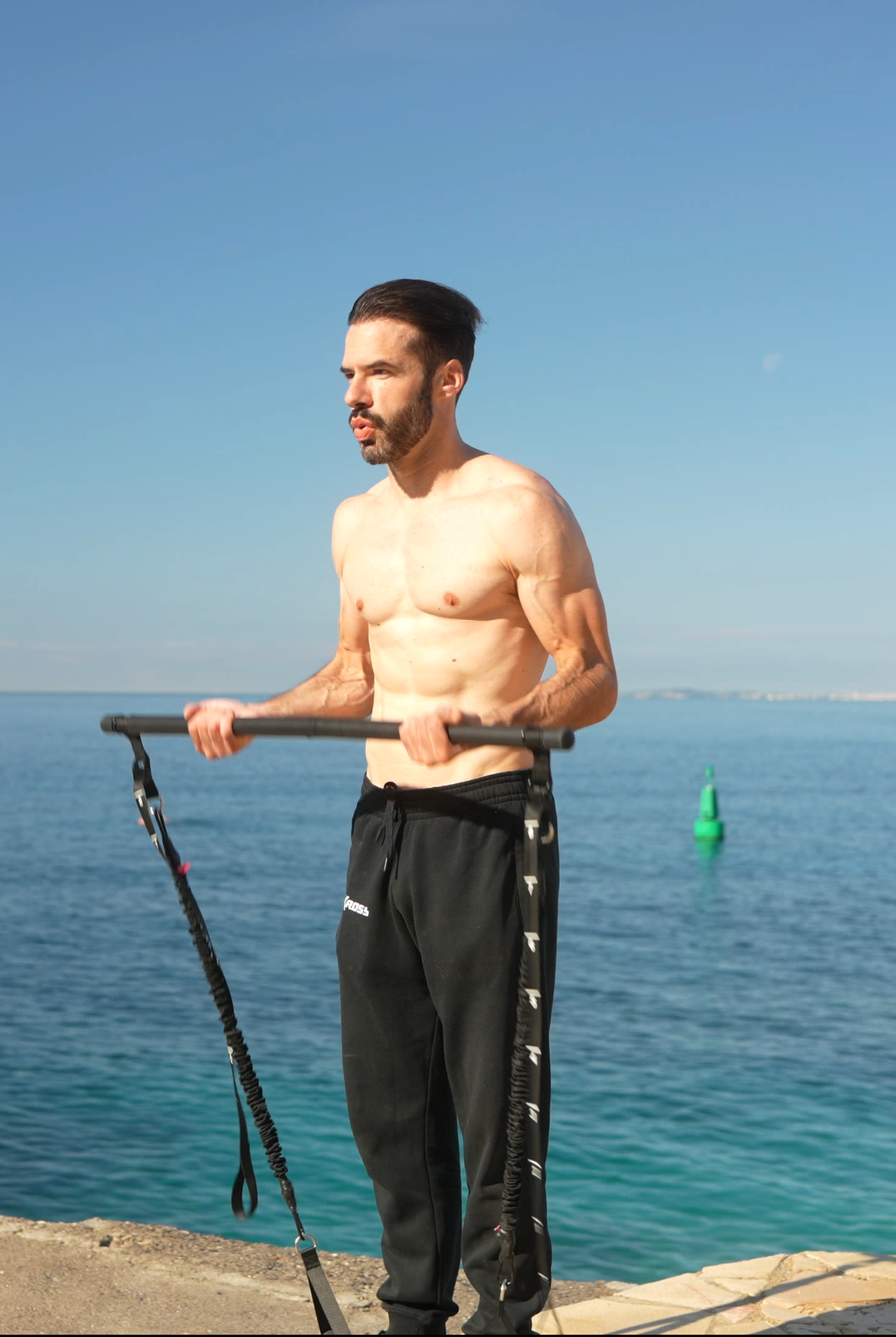 Homme concentré utilisant le pack fitness GymKross pour faire des biceps curls en plein air, sur un tapis de yoga, dans un cadre tranquille avec des arbres en arrière-plan. Il démontre l&#39;efficacité et la commodité de l&#39;équipement GymKross pour un entraînement musculaire n&#39;importe où.