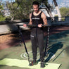 Homme concentré utilisant le pack fitness GymKross pour faire des biceps curls en plein air, sur un tapis de yoga, dans un cadre tranquille avec des arbres en arrière-plan. Il démontre l'efficacité et la commodité de l'équipement GymKross pour un entraînement musculaire n'importe où.