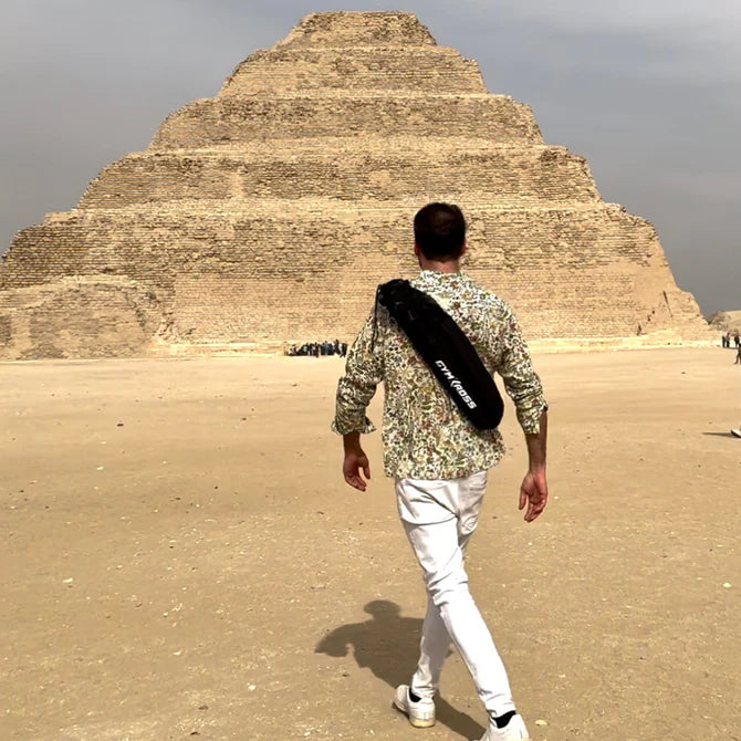 Explorateur portant un sac Gymkross devant la pyramide à degrés de Djoser à Saqqarah, Égypte, symbolisant la fusion de l'histoire ancienne et du fitness moderne.