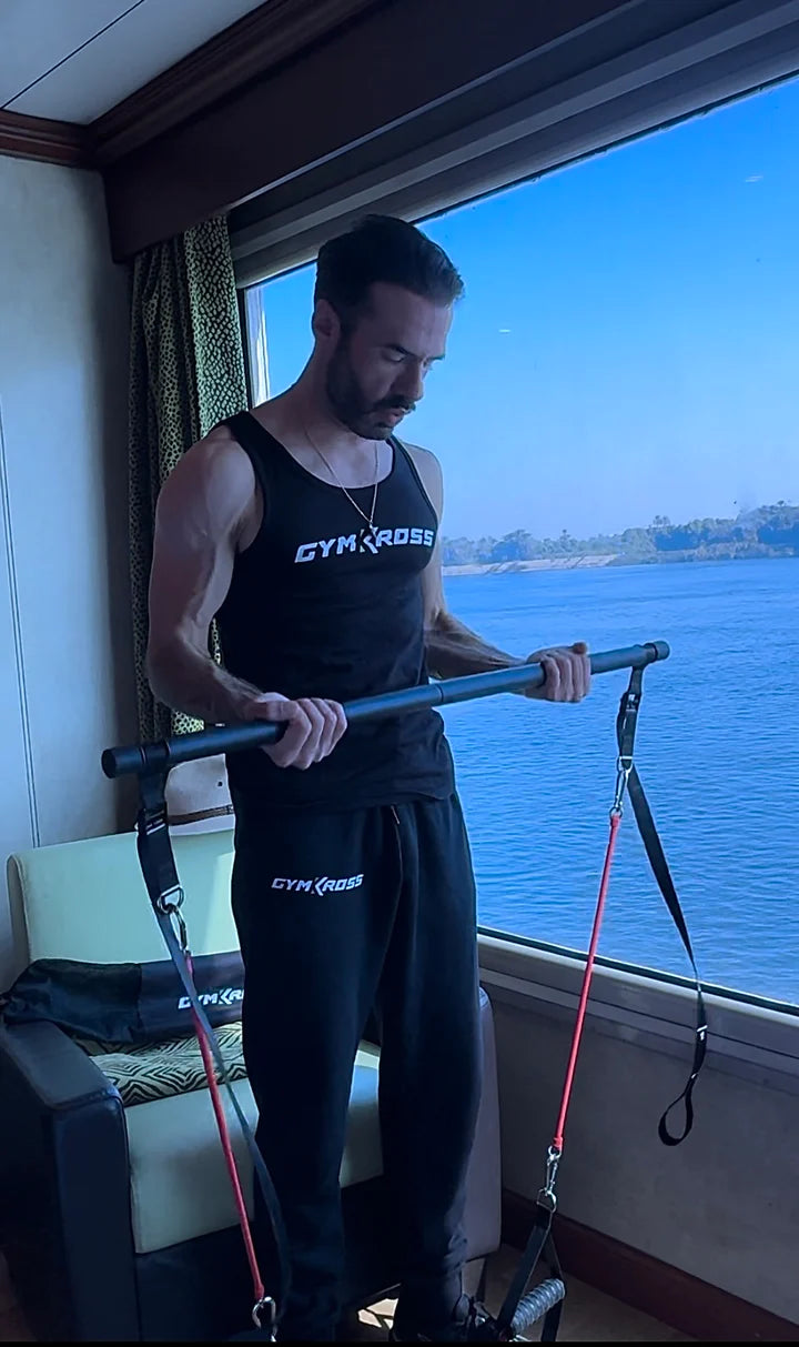 Homme s'entraînant avec l'équipement de fitness GymKross à l'intérieur d'une cabine avec vue sur l'eau, soulignant la facilité d'utilisation et la portabilité de l'équipement pour maintenir une routine d'exercice régulière même en voyage.