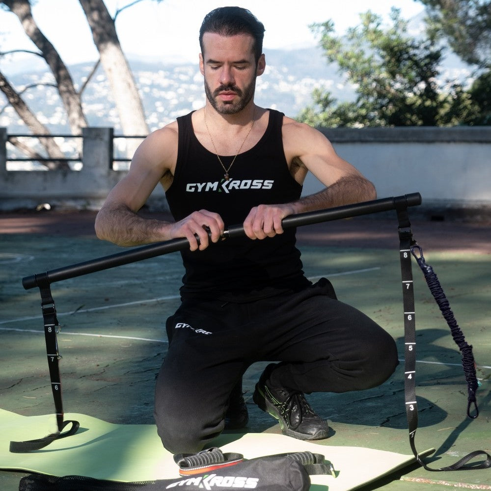 &quot;Homme en tenue GymKross assemblant des équipements de fitness sur un tapis de yoga en extérieur. Vue sur un environnement naturel avec des arbres et des montagnes en arrière-plan.&quot;