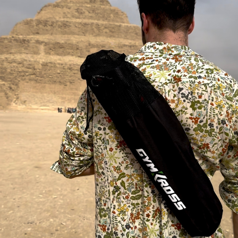 Un homme, vu de dos, portant un sac de transport avec sangle dorsale marqué "GYM KROSS", se tient devant la Pyramide de Djoser à Saqqarah, Égypte. Il est vêtu d'une chemise à motifs floraux, illustrant l'aspect pratique et stylé du sac lors de voyages et d'aventures en plein air.